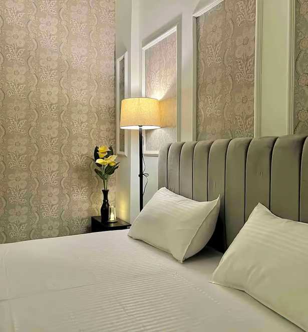 Elegant bedroom with upholstered headboard, decorative wallpaper, wall mouldings and warm ambient lighting.